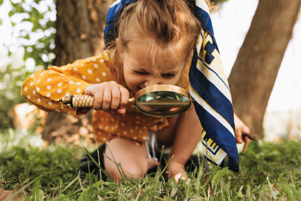 Girl out in the yard looking at the ground through a magnifying glass